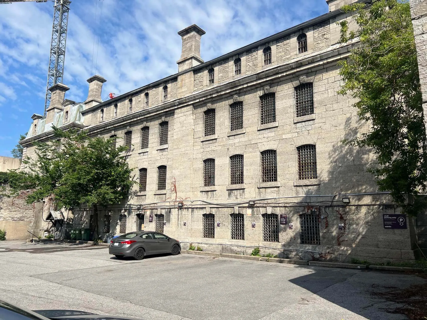 Historic stone building with barred windows and parking lot in front, ivy-covered walls, Ottawa