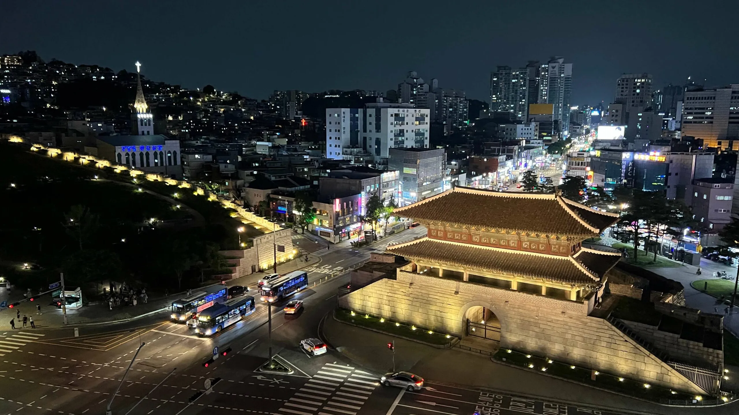 Sungnyemun (Namdaemun) gate lit at night with Seoul cityscape and busy street below