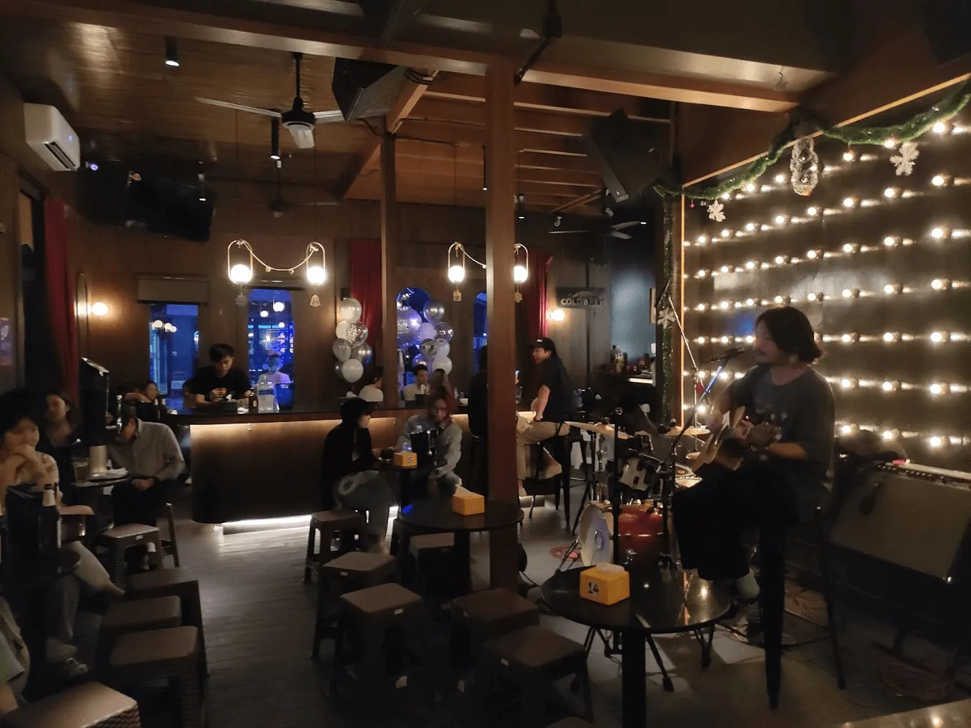 Shelby bar interior with wood ceiling, illuminated mirror vanity, string lights, and patrons at bar and tables