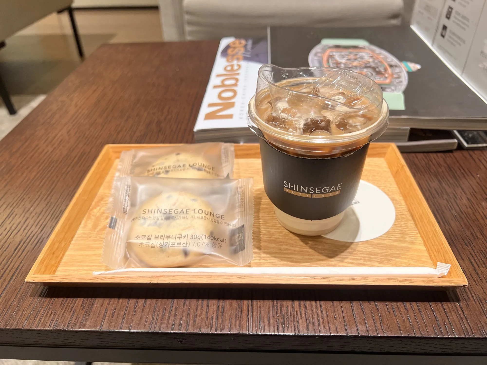 Iced coffee and two Shinsegae Lounge cookies on a wooden tray