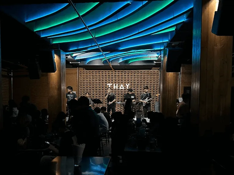 Live band performing on stage at Thay music venue with blue and green neon ceiling lights and brick backdrop