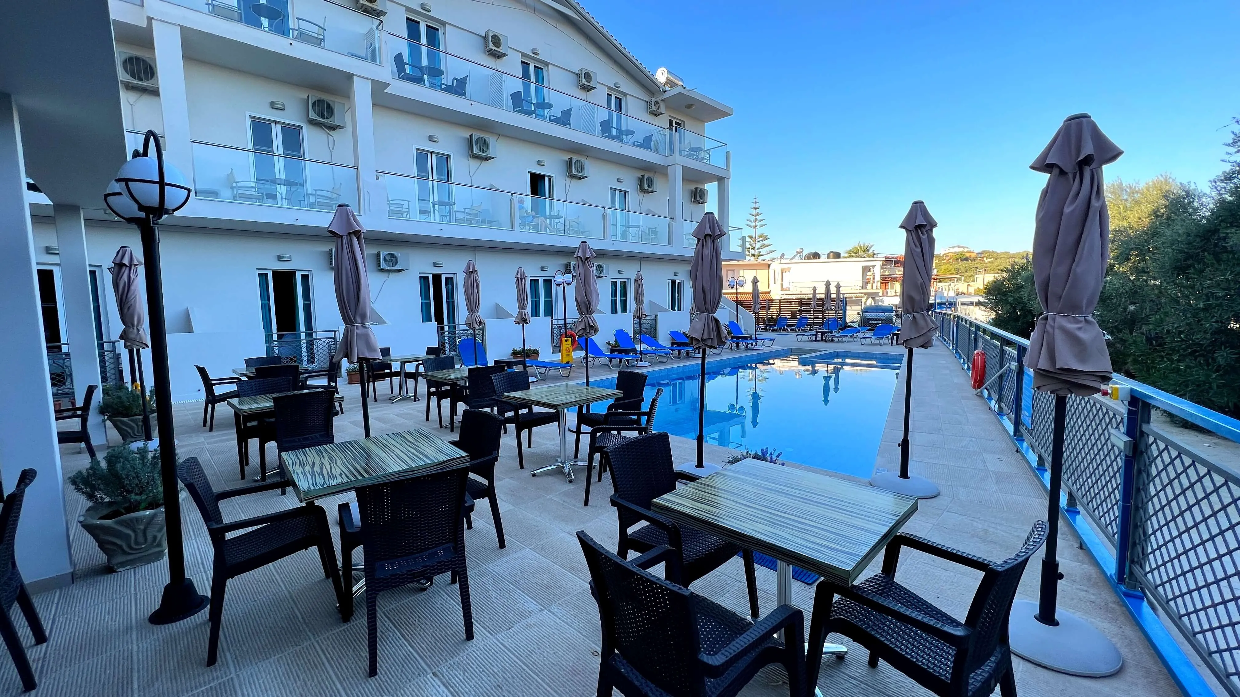 Pool deck at The Senses hotel in Tsilivi with blue swimming pool, black lounge chairs, closed umbrellas, and white apartment building backdrop