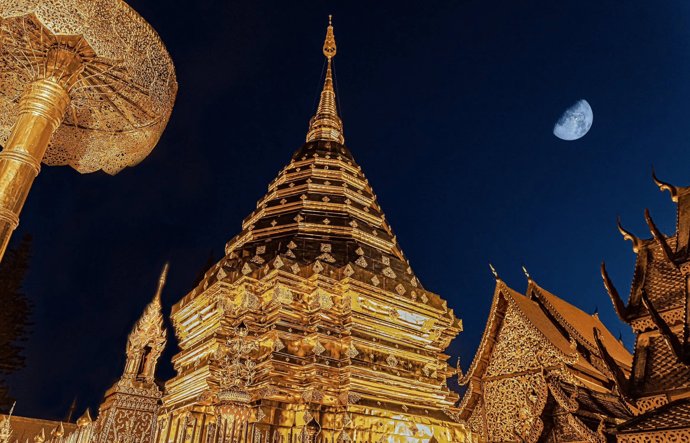 Wat Phra That Doi Suthep golden chedi illuminated at night with moon in deep blue sky, Chiang Mai Thailand