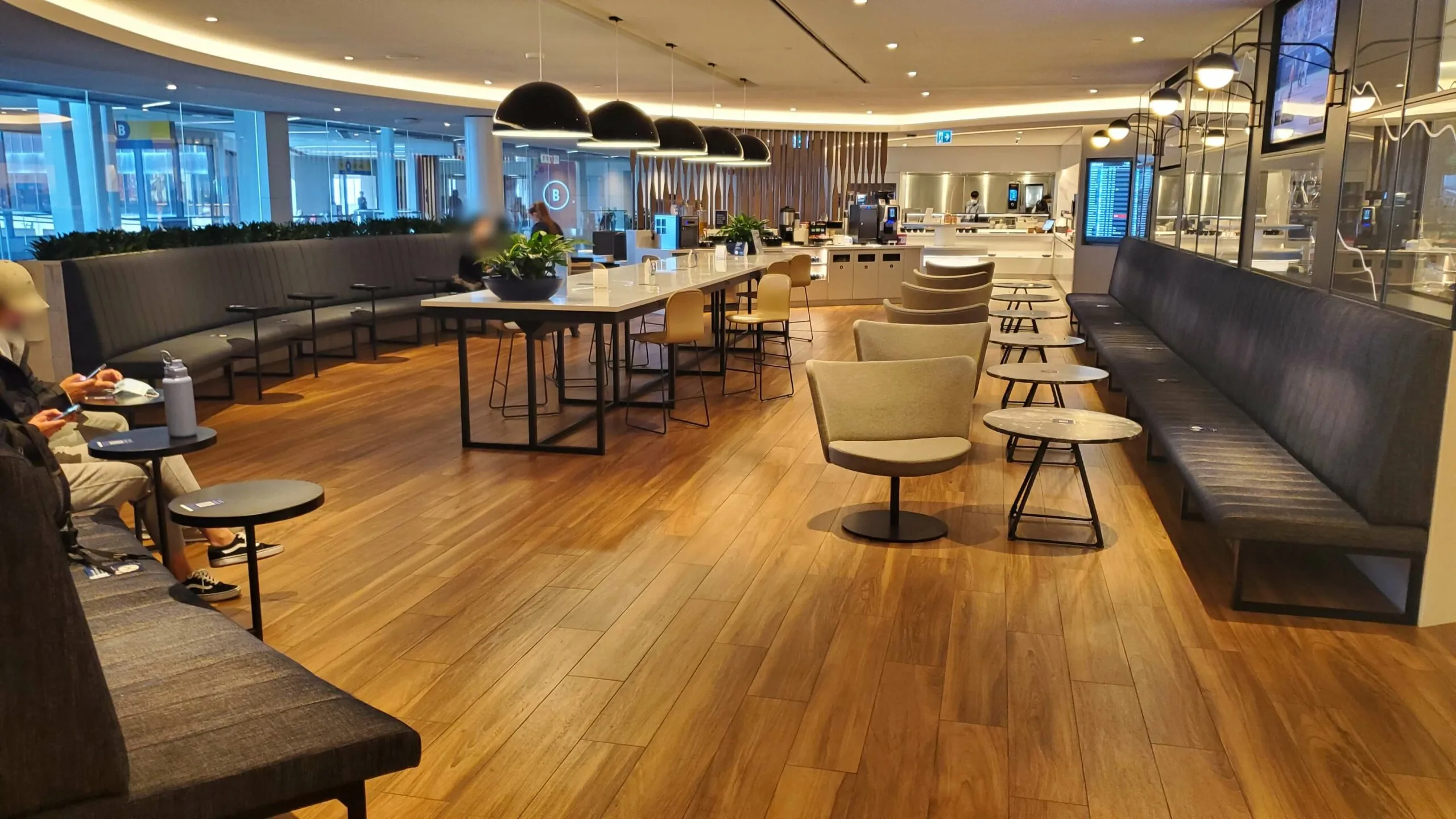 WestJet Elevation Lounge interior with wooden flooring, black leather seating, communal dining table, and floor-to-ceiling windows overlooking a city.
