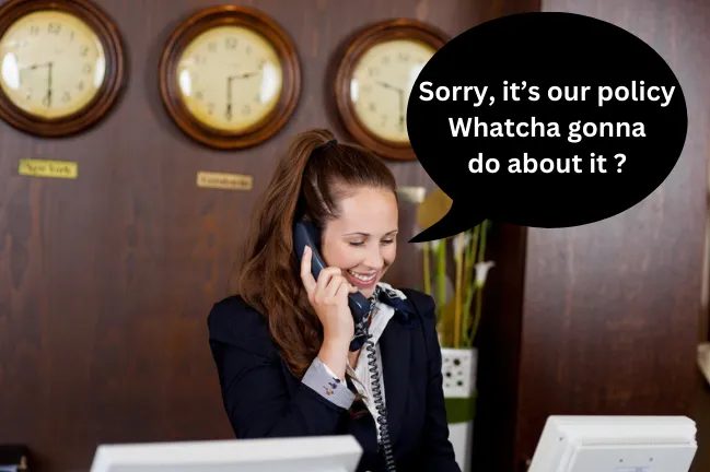 Hotel concierge at desk speaking on phone with world clocks on wall behind her