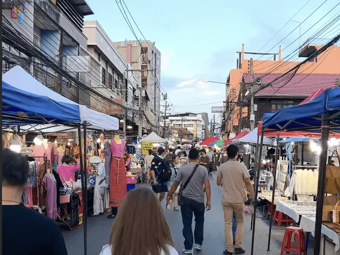 Wualai Street Market with blue vendor tents, clothing stalls, and shoppers in Chiang Mai, Thailand.