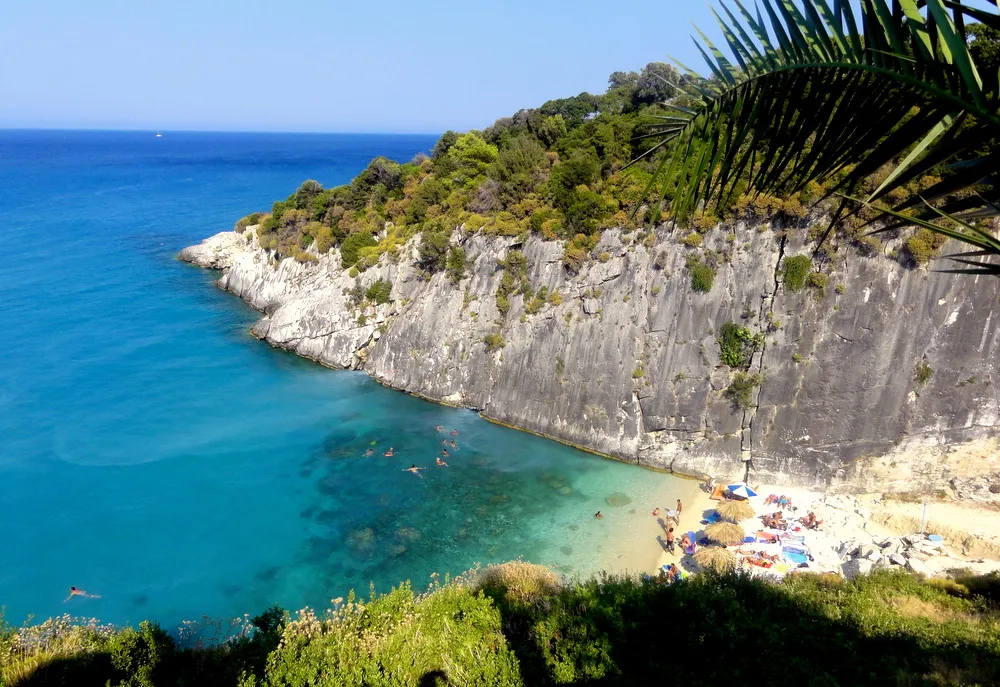 Turquoise Adriatic cove with white limestone cliffs, small sandy beach, and moored boats near Xigia Beach, Croatia
