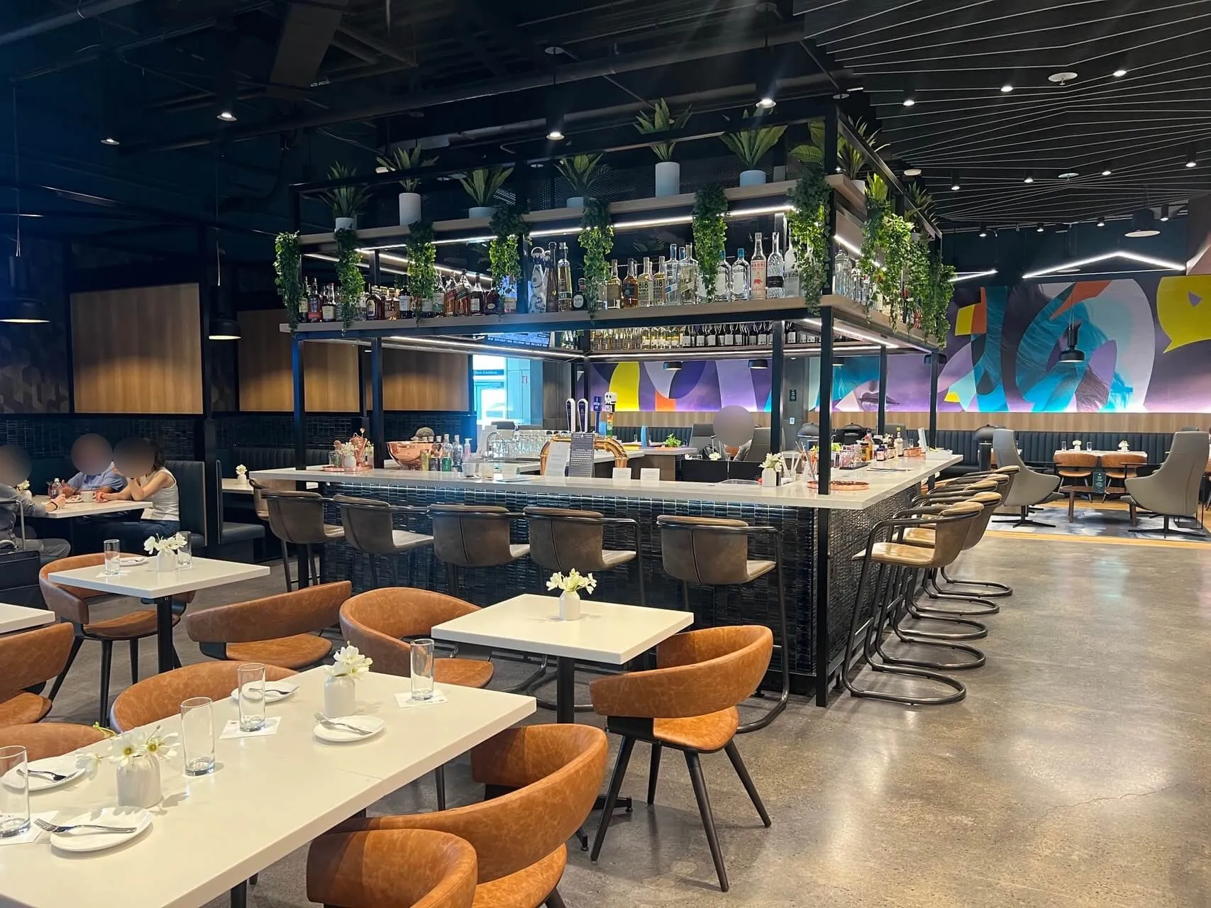 Aspire Lounge dining area with modern bar, hanging plants, orange chairs, and colorful artwork at YYZ Toronto airport