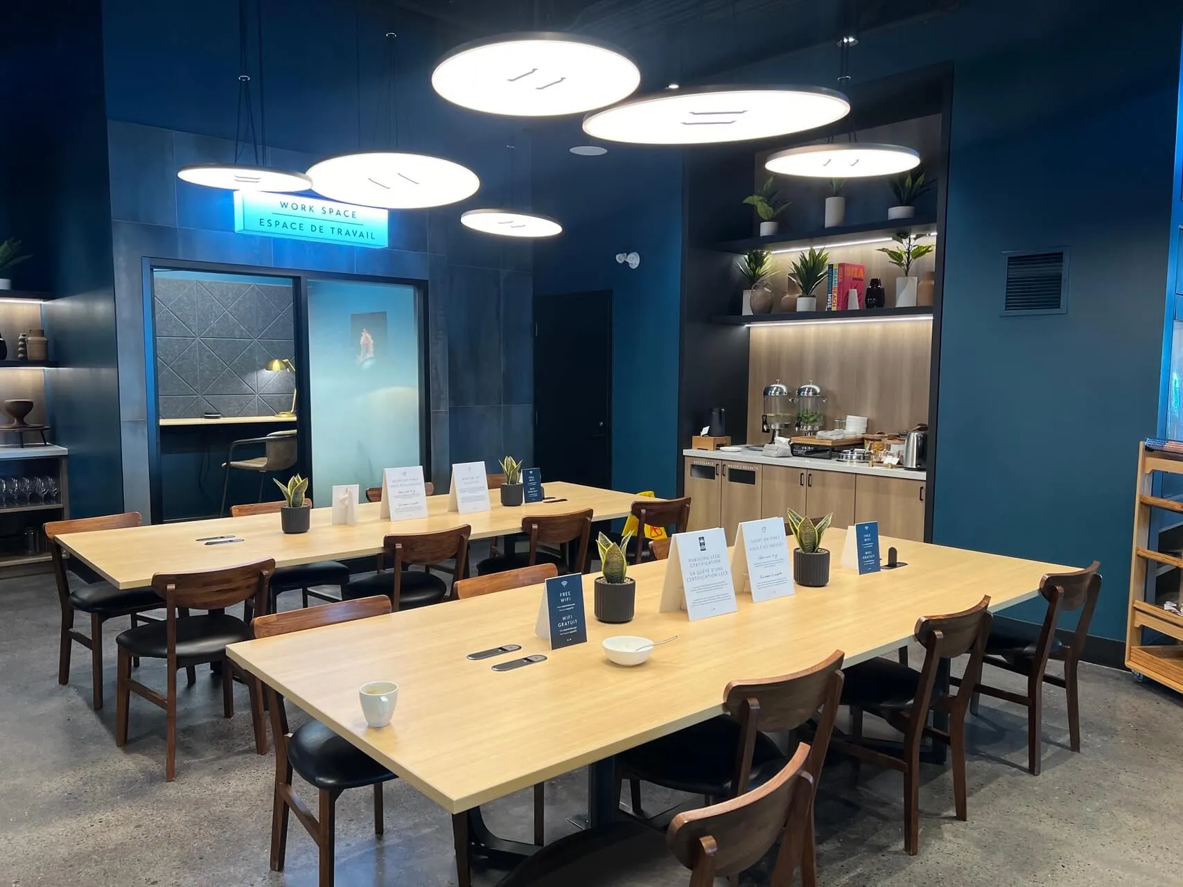 Aspire Lounge work space with wooden tables, modern pendant lighting, and blue accent walls at YTZ Toronto airport.