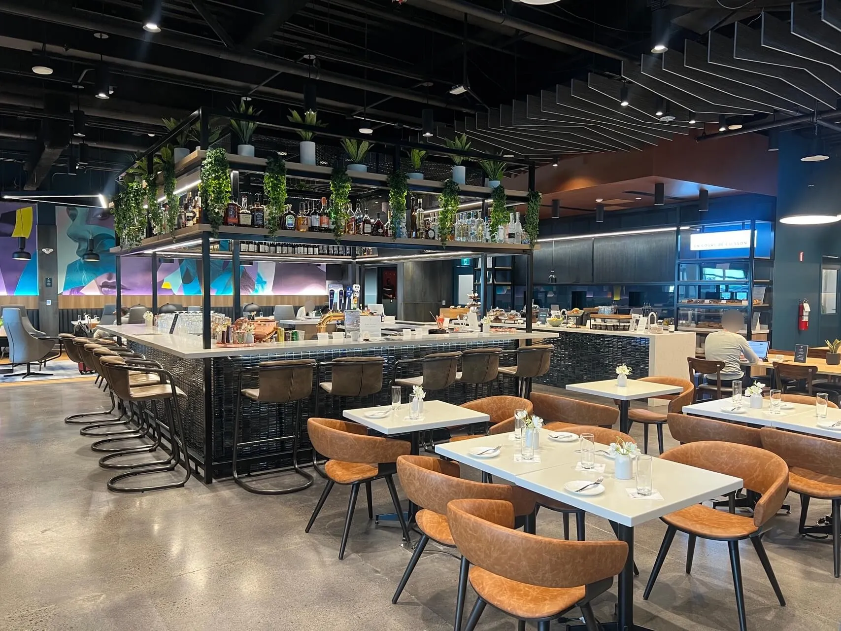 Aspire Lounge dining area with black bar, hanging plants, and orange chairs at Toronto Pearson airport