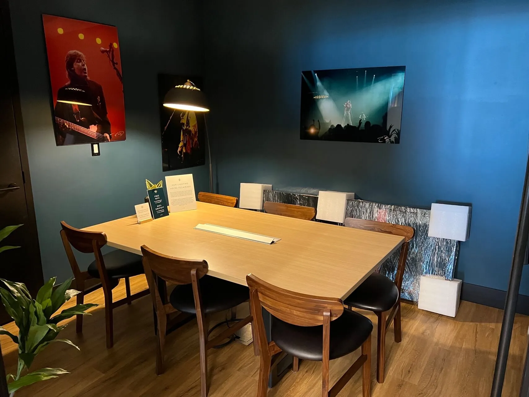 Modern meeting room with wooden table, mid-century chairs, and concert photography on teal accent walls at YYZ Aspire Lounge.