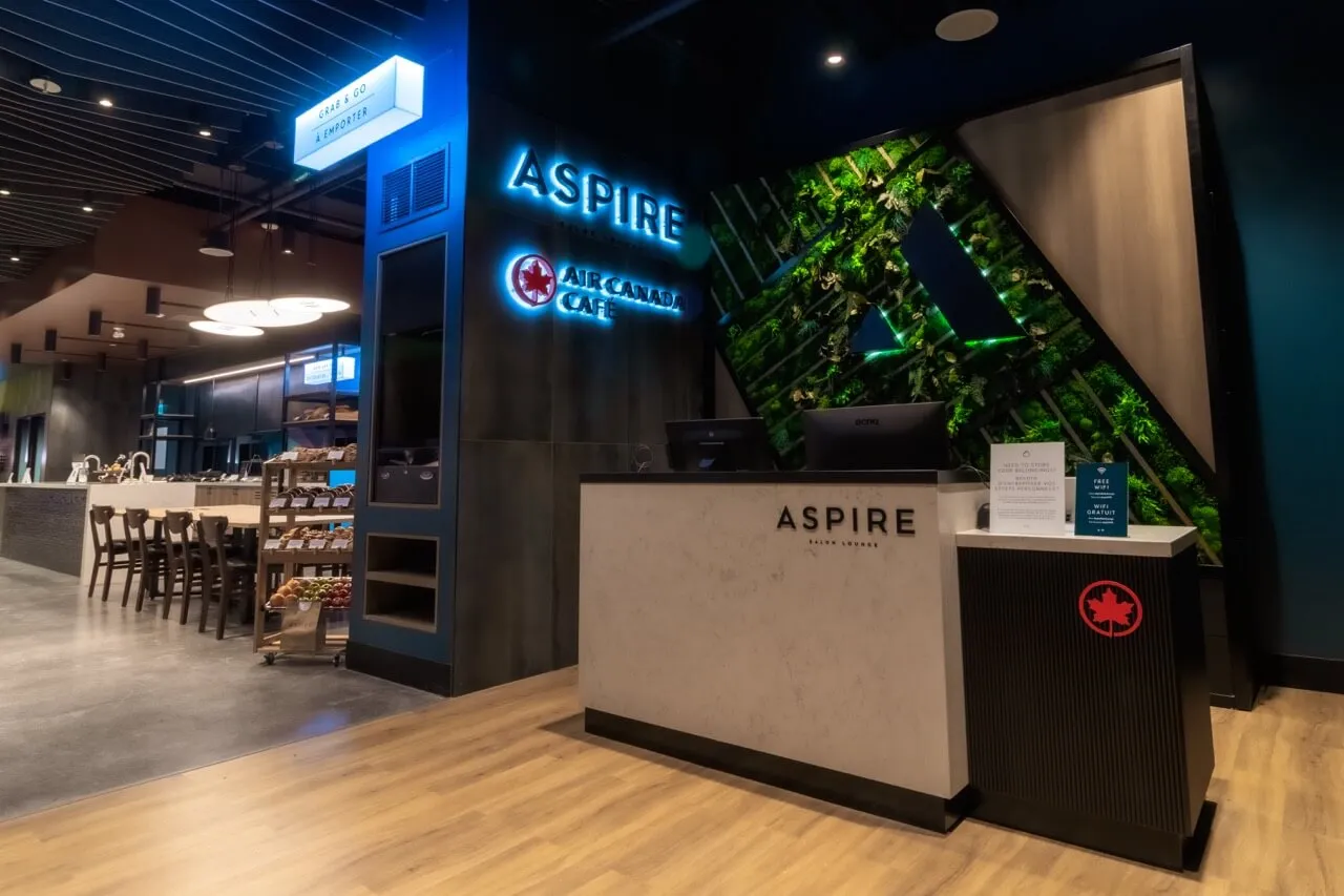Aspire lounge reception desk with neon signage and living plant wall at Toronto Pearson airport