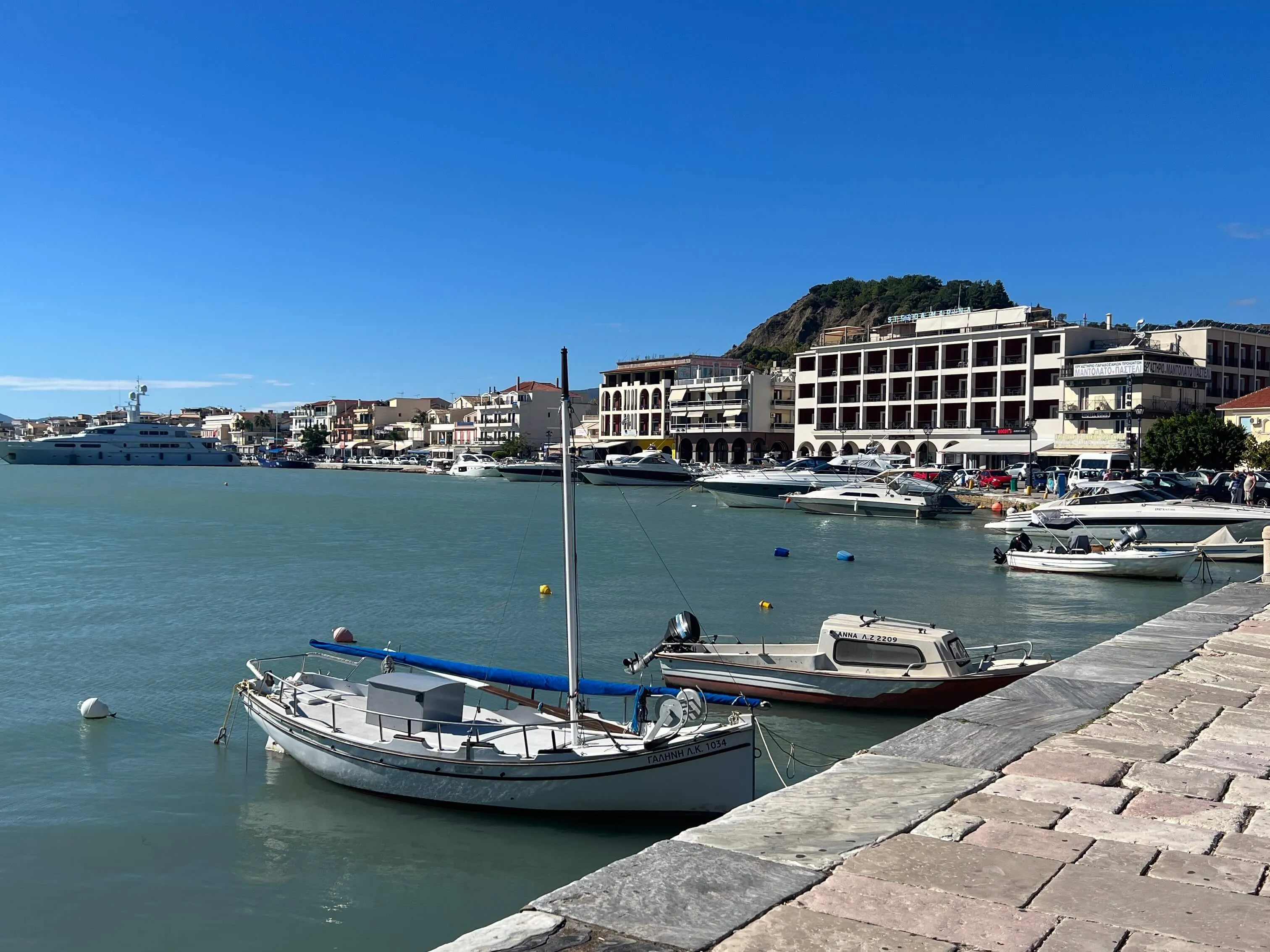 Fishing boats moored in turquoise harbor at Zante Town waterfront with buildings and hillside backdrop